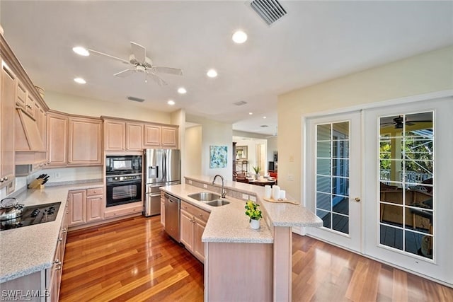 kitchen featuring light brown cabinetry, french doors, sink, black appliances, and an island with sink