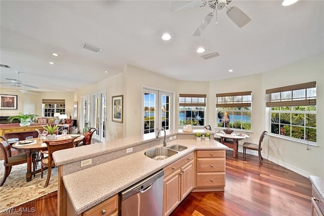 kitchen featuring light brown cabinetry, stainless steel dishwasher, a kitchen island with sink, dark wood-type flooring, and sink