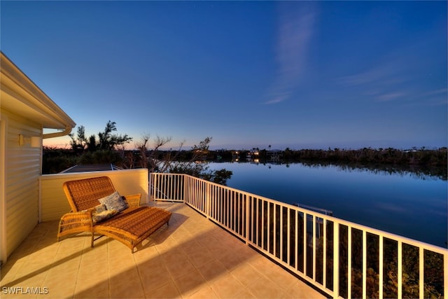 patio terrace at dusk featuring a water view and a balcony