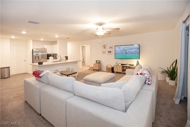 carpeted living room with ceiling fan and sink