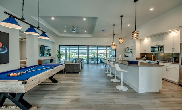 recreation room with a raised ceiling, ceiling fan, light hardwood / wood-style flooring, a high ceiling, and pool table