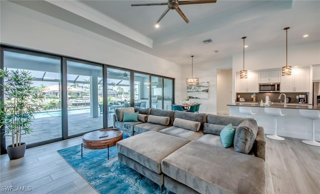 living room featuring ceiling fan, sink, light hardwood / wood-style flooring, a tray ceiling, and ornamental molding