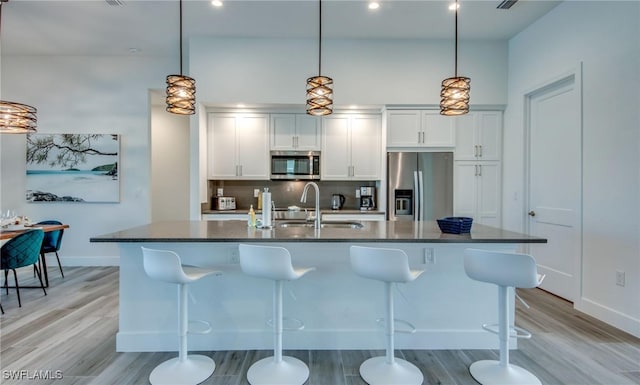 kitchen featuring a center island with sink, sink, stainless steel appliances, and hanging light fixtures