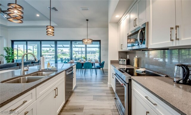 kitchen with light stone counters, white cabinetry, hanging light fixtures, and appliances with stainless steel finishes