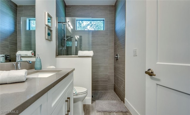 bathroom featuring a tile shower, vanity, hardwood / wood-style flooring, and toilet