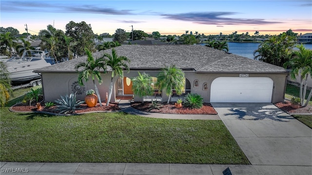 ranch-style home with a lawn, a water view, and a garage