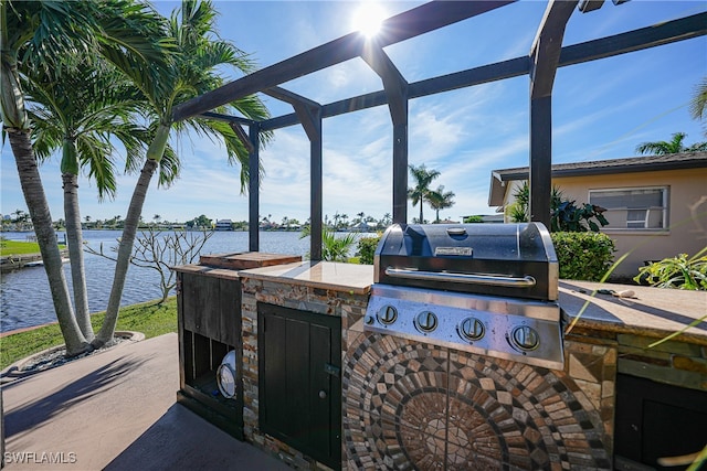 view of patio / terrace featuring grilling area, a water view, exterior kitchen, and glass enclosure