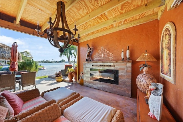 living area featuring an inviting chandelier, concrete floors, a water view, beamed ceiling, and a tiled fireplace