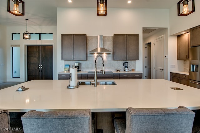 kitchen featuring decorative light fixtures, a kitchen bar, wall chimney range hood, and a kitchen island with sink