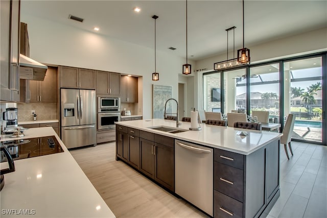 kitchen with dark brown cabinets, stainless steel appliances, sink, decorative light fixtures, and a center island with sink