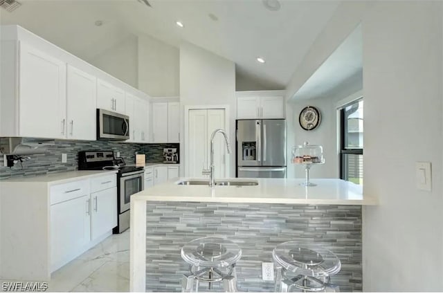 kitchen with backsplash, vaulted ceiling, sink, white cabinetry, and appliances with stainless steel finishes