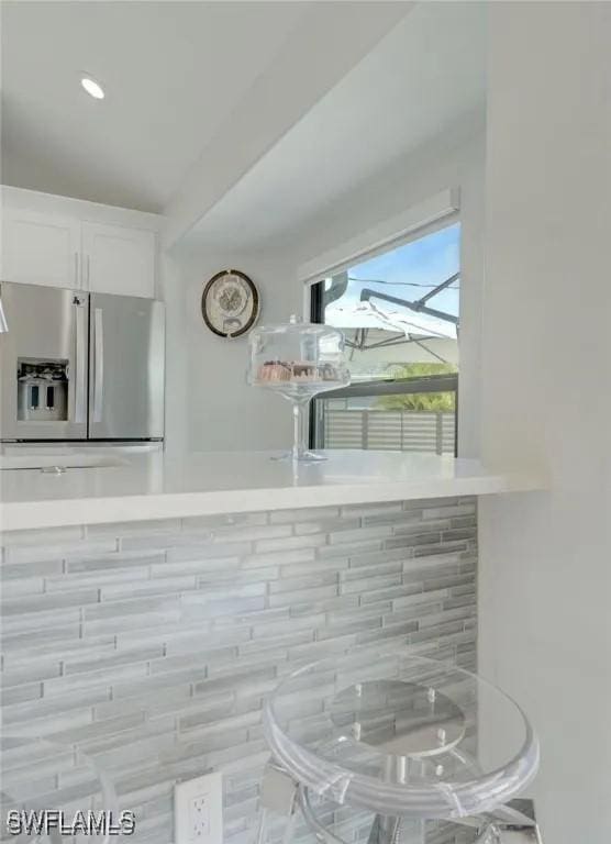 kitchen with stainless steel refrigerator with ice dispenser, decorative backsplash, and white cabinets