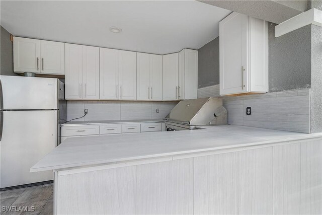 kitchen with kitchen peninsula, backsplash, white fridge, and white cabinets