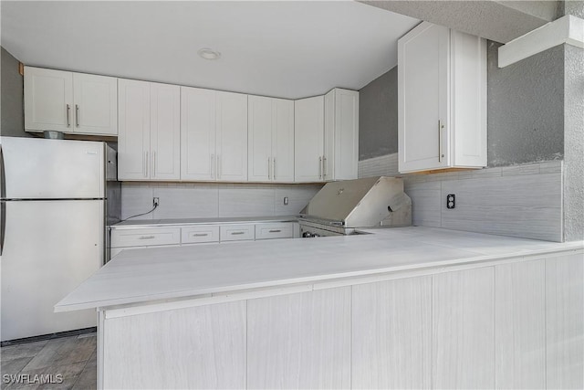 kitchen with decorative backsplash, kitchen peninsula, white cabinets, and refrigerator