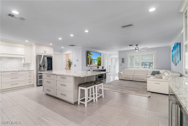 kitchen with light stone countertops, stainless steel refrigerator with ice dispenser, a kitchen breakfast bar, a kitchen island, and white cabinetry