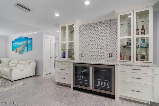 bar with wine cooler, white cabinetry, and light stone counters