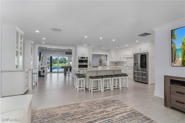 kitchen featuring a large island, stainless steel appliances, a kitchen breakfast bar, backsplash, and white cabinets