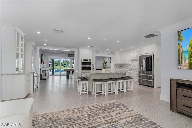 kitchen with a breakfast bar, tasteful backsplash, white cabinets, stainless steel appliances, and a spacious island