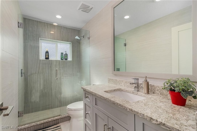 bathroom featuring vanity, toilet, a shower with door, and tile walls