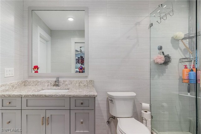 bathroom with vanity, toilet, a shower with shower door, and tile walls