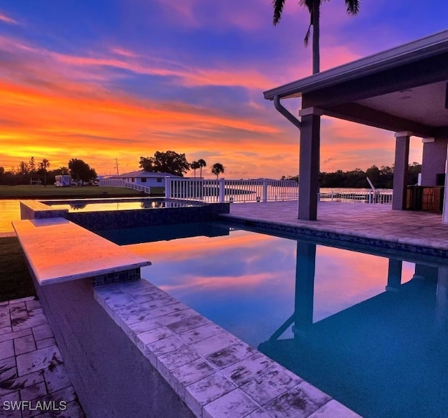 pool at dusk featuring exterior bar, a patio area, and a water view