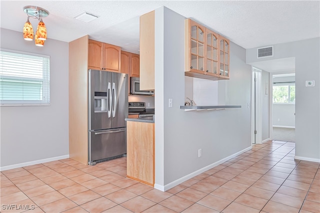 kitchen featuring a wealth of natural light, a textured ceiling, stainless steel appliances, and hanging light fixtures