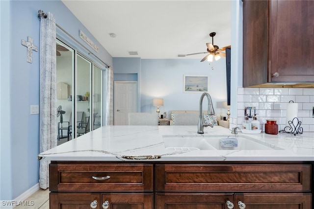 kitchen featuring sink, decorative backsplash, ceiling fan, light stone countertops, and dark brown cabinets