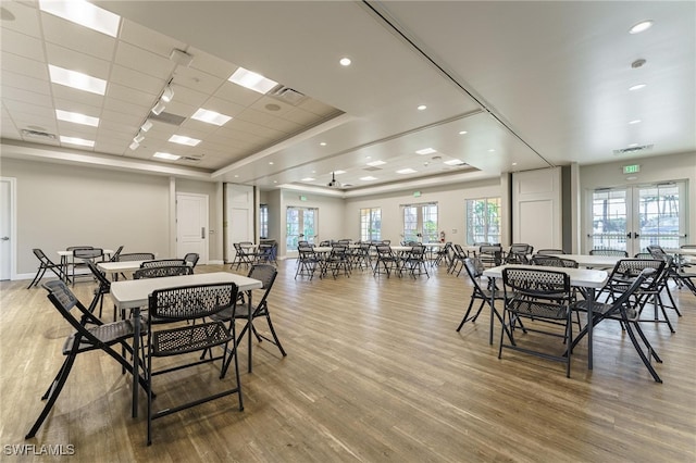 dining space with french doors, a tray ceiling, and light hardwood / wood-style flooring