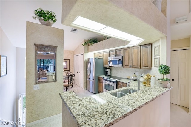 kitchen with sink, light stone counters, high vaulted ceiling, kitchen peninsula, and appliances with stainless steel finishes