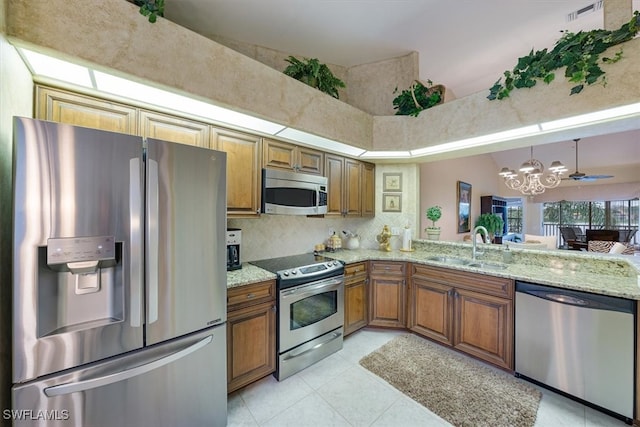 kitchen featuring sink, hanging light fixtures, stainless steel appliances, light stone counters, and ceiling fan with notable chandelier