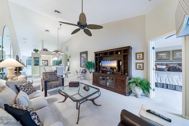 carpeted living room with ceiling fan with notable chandelier and high vaulted ceiling