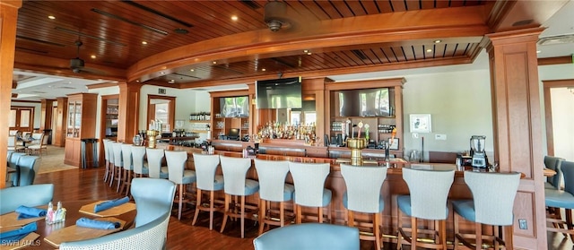 bar featuring ornate columns, wooden ceiling, beamed ceiling, and wood-type flooring