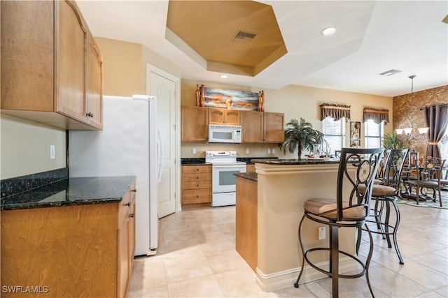 kitchen featuring white appliances, dark stone counters, a tray ceiling, light tile patterned flooring, and a kitchen bar