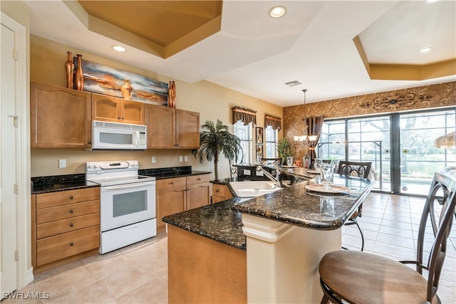 kitchen with white appliances, sink, an island with sink, a tray ceiling, and decorative light fixtures