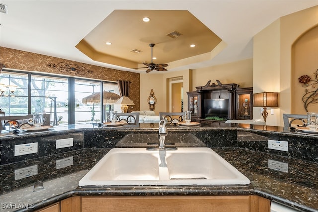 kitchen with a tray ceiling, dark stone counters, and sink