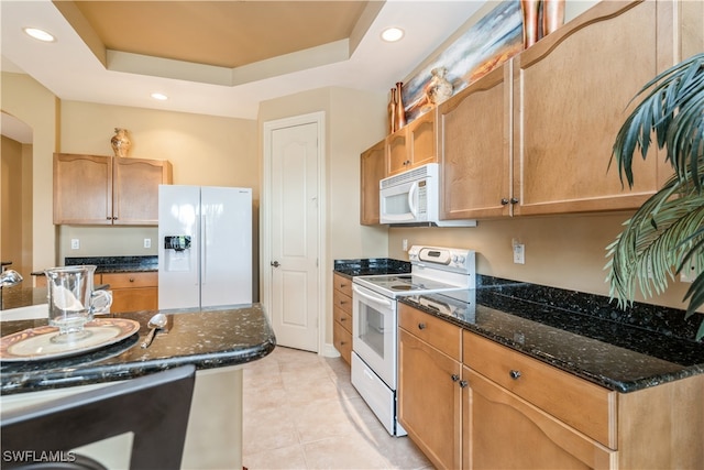 kitchen with white appliances, a raised ceiling, and dark stone counters