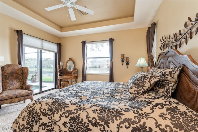 carpeted bedroom featuring a tray ceiling, access to exterior, and ceiling fan