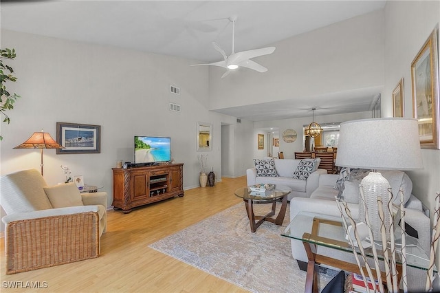 living room with ceiling fan with notable chandelier, high vaulted ceiling, and light hardwood / wood-style flooring