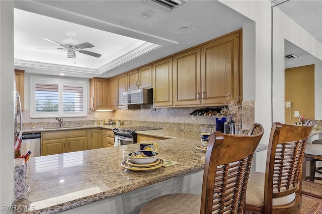 kitchen featuring kitchen peninsula, appliances with stainless steel finishes, light stone counters, a raised ceiling, and sink