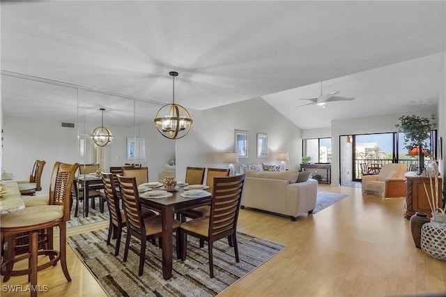 dining space with ceiling fan with notable chandelier, light wood-type flooring, and vaulted ceiling