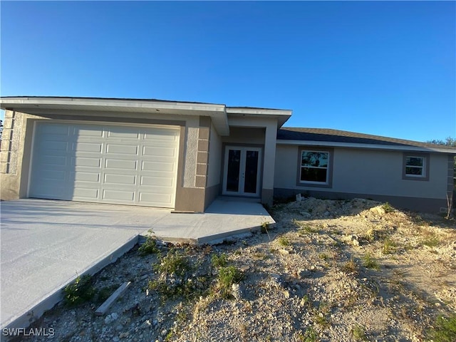 view of front of house featuring french doors, a garage, driveway, and stucco siding