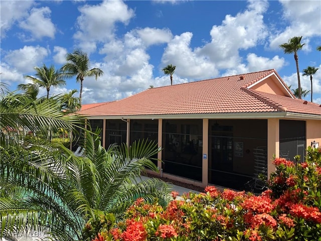 rear view of property featuring a sunroom, a tiled roof, and stucco siding