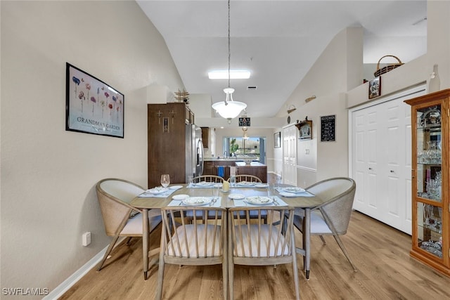 dining room featuring high vaulted ceiling and light hardwood / wood-style flooring