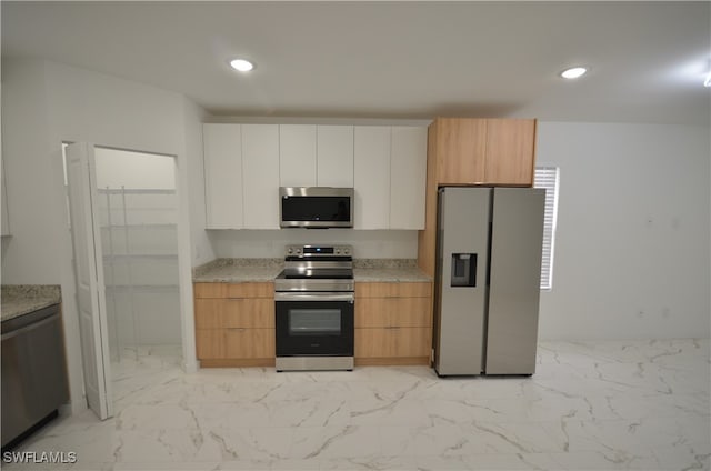 kitchen with light stone counters, white cabinetry, stainless steel appliances, and light brown cabinetry