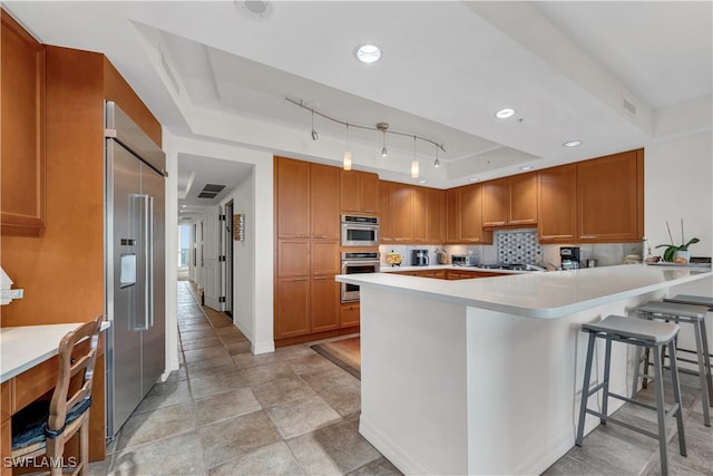 kitchen featuring a kitchen breakfast bar, appliances with stainless steel finishes, tasteful backsplash, a tray ceiling, and kitchen peninsula