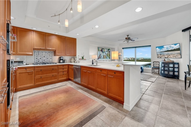 kitchen with decorative backsplash, kitchen peninsula, a tray ceiling, stainless steel appliances, and sink