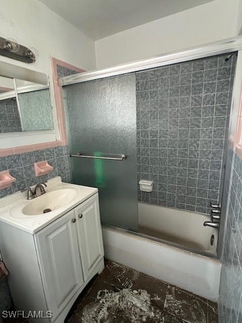 bathroom featuring combined bath / shower with glass door, decorative backsplash, vanity, and tile walls