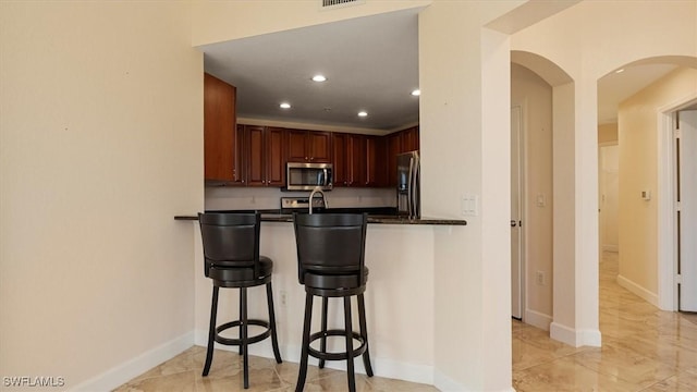 kitchen with dark countertops, recessed lighting, stainless steel appliances, a peninsula, and a breakfast bar area