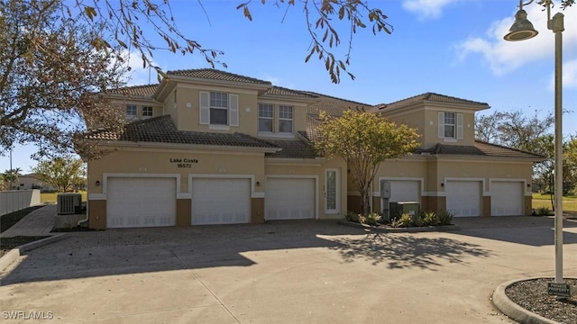 view of front facade featuring stucco siding, central air condition unit, an attached garage, and driveway