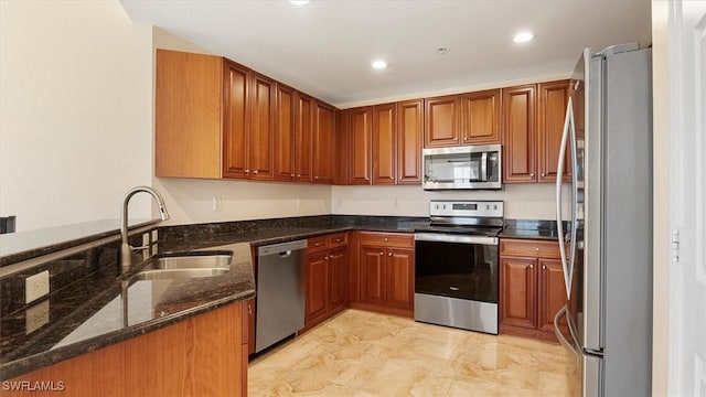 kitchen featuring dark stone countertops, appliances with stainless steel finishes, brown cabinets, and a sink